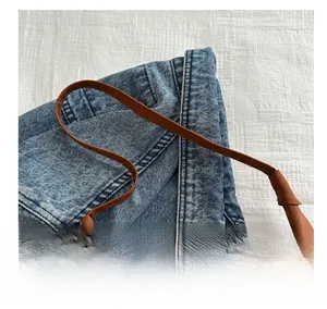 Detailed close-up of brown leather strap and washed blue denim fabric on tote bag