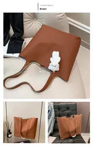 Detail view of large brown lychee grain leather tote bag with cute white bear charm