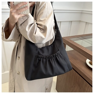 Detail of black pleated nylon crossbody bag shown on a beige trench coat outfit
