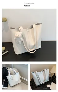 Detail of white pebbled leather tote bag with plush bear charm and magnetic buckle