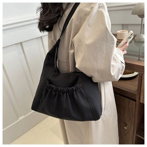Detail of minimalist black pleated crossbody bag styled with a beige trench coat
