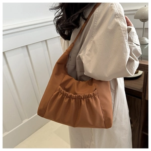 Detail of a brown pleated nylon tote bag with textured surface shown on a model