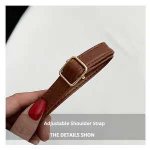 Detail of brown faux leather adjustable shoulder strap with gold metal buckle