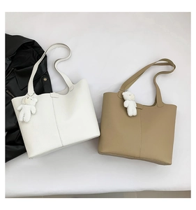 Detail of lychee pattern leather tote bags in white and khaki with plush bear charms