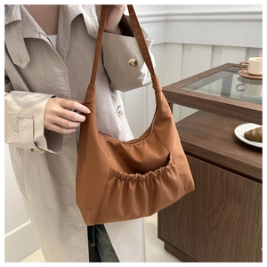 Brown oversized tote bag with pleated front pocket shown in a lifestyle street setting
