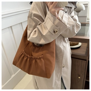 Brown nylon hobo shoulder bag with pleated front pocket shown on a model's shoulder