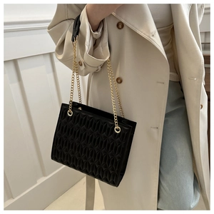 Close-up of quilted black tote bag with gold chain strap worn on a beige trench coat