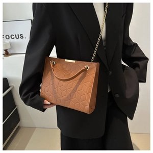 Detail of brown quilted leather bag with elegant gold chain strap worn on stylish outfit