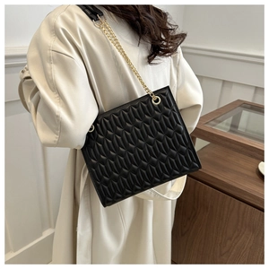 Detail of black quilted shoulder bag with gold chain strap on a beige trench coat