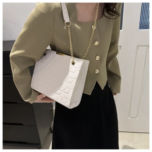Close-up of a white quilted crossbody bag with gold chain strap on a green suit
