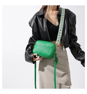Green textured camera bag detail showing geometric wide strap and tassel leather strap