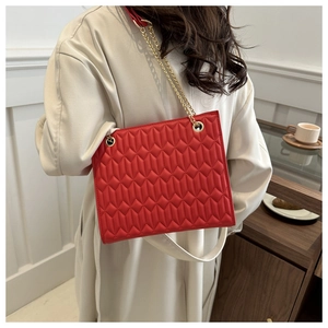 Detail of red quilted tote bag with gold chain strap and geometric stitching texture