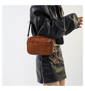 Detail of brown faux leather camera bag with V-shaped stitching and woven shoulder strap