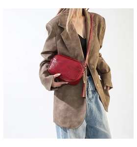 Détail du sac bandoulière vintage en cuir rouge avec surpiqûres en V et pompon déco
