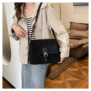 Detail of a black faux suede crossbody bag featuring a golden horseshoe buckle