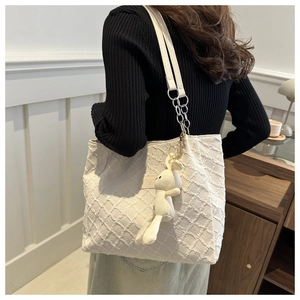 Detail of cream tote bag featuring quilted texture, chain strap, and cute plush rabbit charm