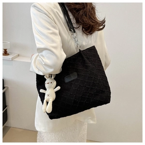 Detail of quilted black tote bag featuring metallic chain strap and plush rabbit charm