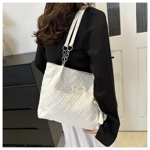 Detail of white quilted tote bag with textured fabric, leather logo, and chain strap