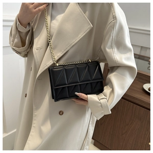 Detail of black quilted leather shoulder bag with gold chain strap on a trench coat