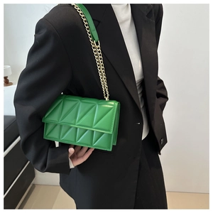 Detail of green quilted crossbody bag with gold chain strap worn with a black blazer