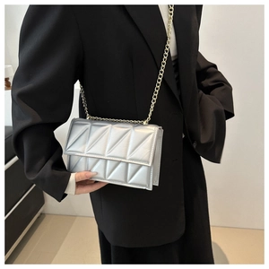 Detail of silver crossbody bag with geometric quilting and gold chain on a model
