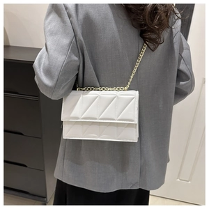 Chic white quilted chain bag with triangular stitching worn as a crossbody purse
