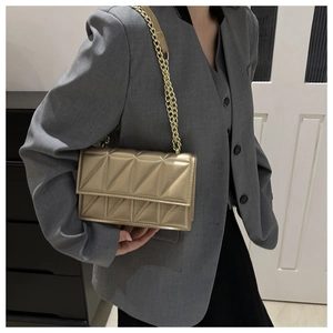 Detail of champagne gold quilted crossbody bag with gold chain strap worn on dark blazer