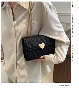 Detail of heart-quilted black PU leather bag with golden heart buckle and chain strap