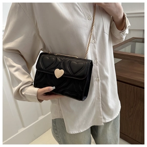 Close-up of black heart quilted handbag featuring a golden heart buckle and chain strap