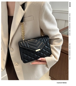 Detail of black quilted crossbody bag with gold chain strap on a blazer outfit