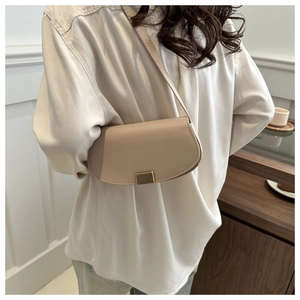Detail of minimalist beige half-moon bag with textured gold magnetic buckle on a model