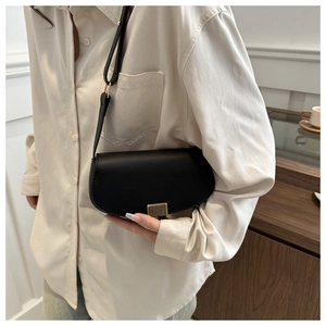 Detail of black saddle bag with gold vertical clasp and adjustable leather shoulder strap