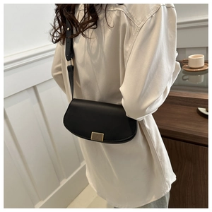 Side view of black crescent leather bag with gold buckle on a person's shoulder