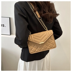 Détail d'un sac bandoulière matelassé beige avec chaîne dorée sur un mannequin