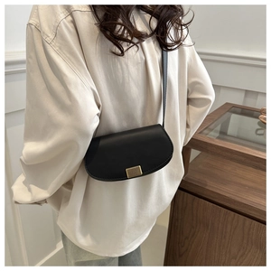 Detail of black leather saddle bag featuring a textured gold metal buckle and slim strap