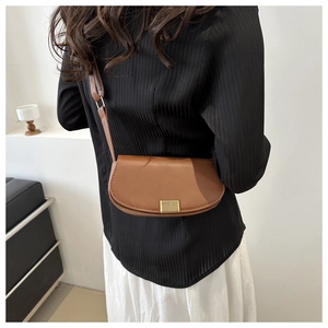 Rear view of a model wearing a brown saddle bag with a golden striped metal buckle
