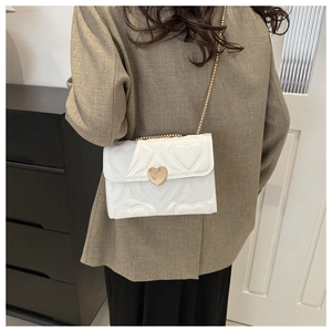 White heart quilted leather bag on model with gold chain strap and heart buckle