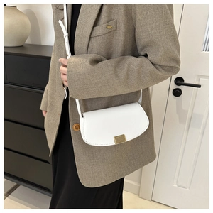 Detailed view of a white PU saddle bag with a minimalist gold buckle on a brown suit jacket