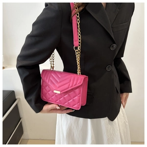 Detailed view of rose red quilted crossbody bag with gold buckle on a model's outfit