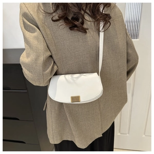 White leather saddle bag with gold buckle shown on shoulder of a model in brown suit