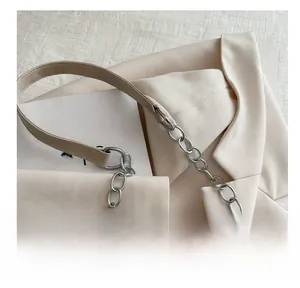 Dettaglio borsa tote in pelle beige con catena d'argento e occhielli metallici moderni