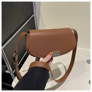 Close-up of brown saddle bag with matte PU leather texture and vertical gold clasp