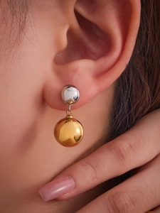 Macro detail of two-tone hollow steel ball drop earrings in polished 18k gold and silver