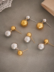 Detailed view of polished gold and silver double bead earrings on a grey textured background