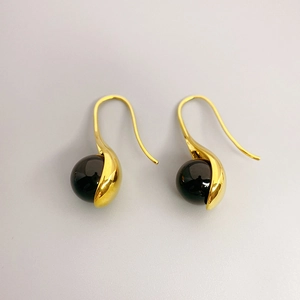 Detailed close-up of gold-plated drop earrings featuring black agate and white pearl accents