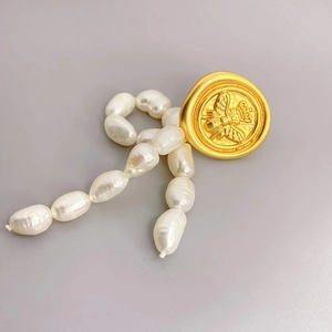 Baroque pearl necklace with vintage gold bee relief pendant on a minimalist grey background