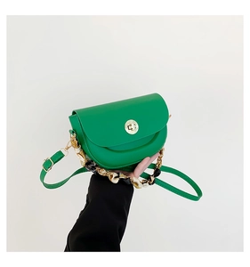 Detail of green saddle bag with golden circular twist lock and scarf-wrapped chain strap
