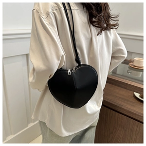 Detail of a black heart-shaped crossbody bag worn by a model in a minimalist setting