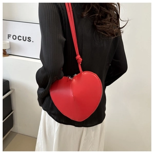 Detail view of a red heart-shaped leather crossbody bag worn on a woman's shoulder