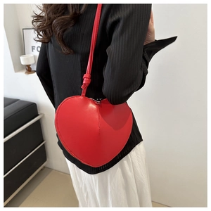 Detail of red heart-shaped leather crossbody bag with silver zipper on a model